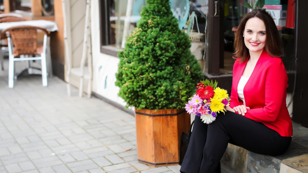 Smiling woman in red blazer with bouquet of flowers on her lap
