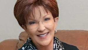 Woman in black blazer with black and white neckerchief and glasses