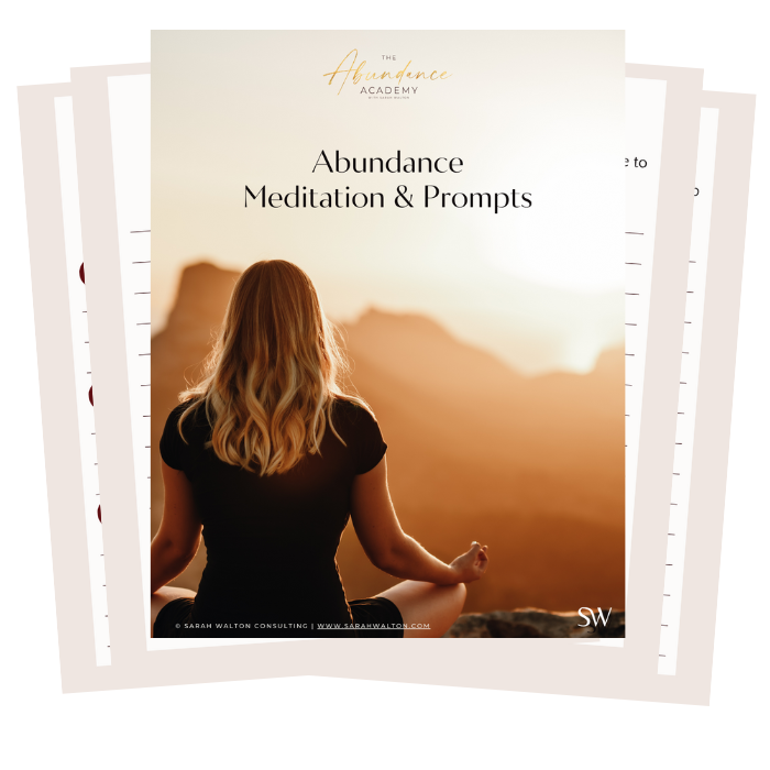 Woman sitting cross-legged with hands on knees facing away from camera doing meditation viewing a sunrise over a mountain range with text Abundance Academy with Sarah Walton Abundance Meditation & Prompts