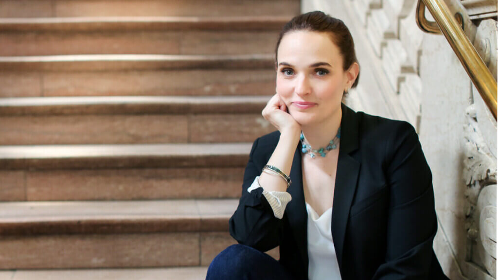 woman in black blazer and white blouse sitting on stairs with right palm under her chin