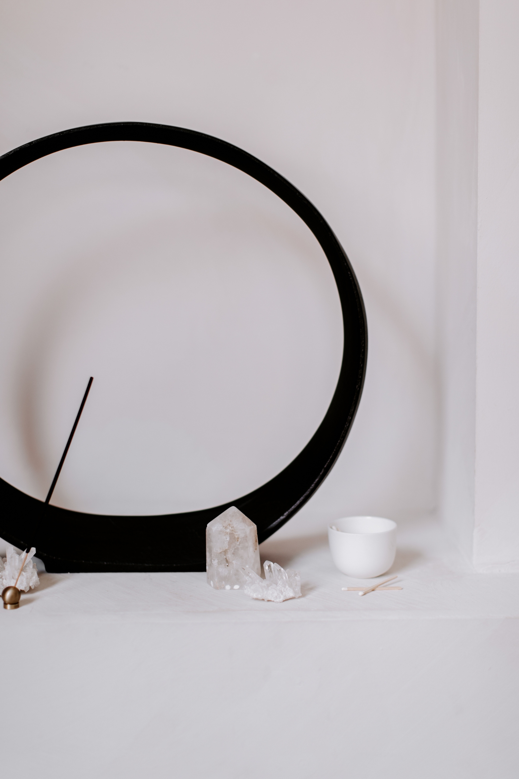 A black ring-shaped incense stand with a quartz crystal cluster on a white shelf