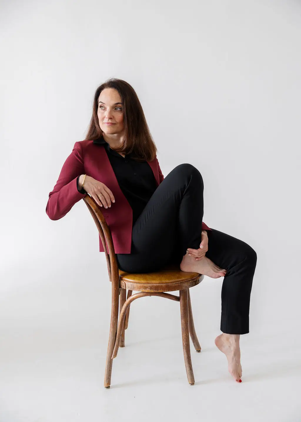Sarah Walton wearing a burgundy blazer sitting in a chair on a white background