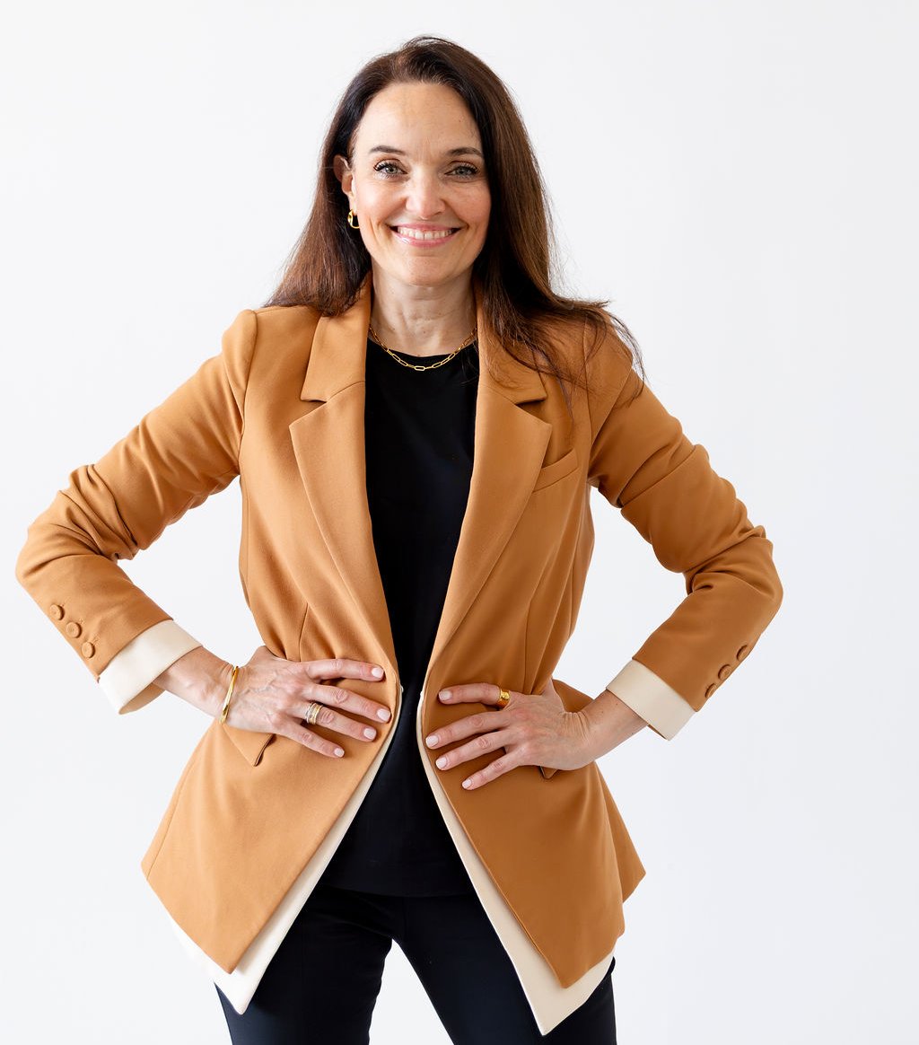 Sarah Walton standing with her hands on her hips, wearing a tan blazer over a black outfit.