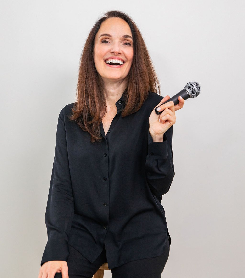 Sarah Walton smiling in a black outfit while holding a microphone.
