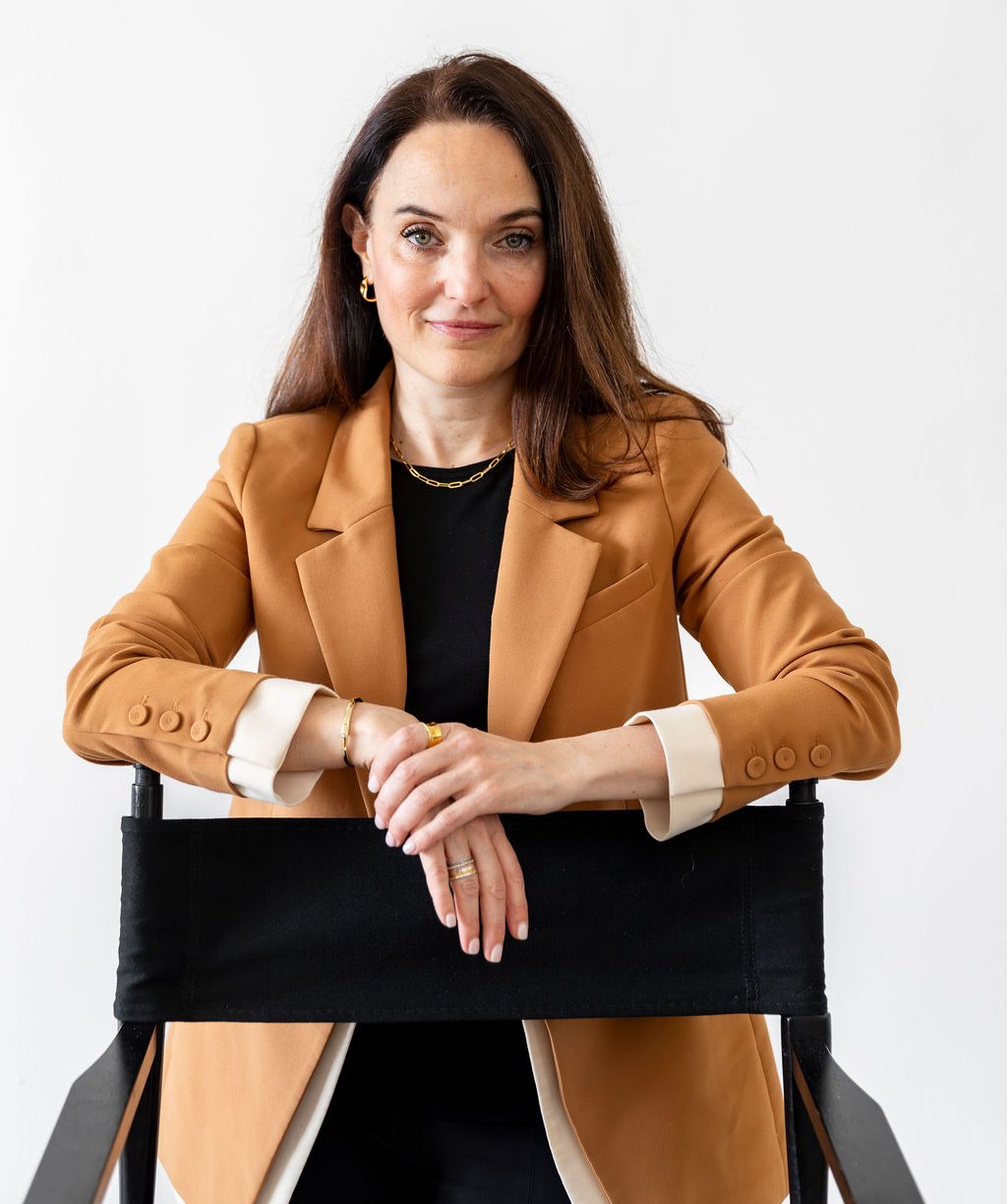 Sarah Walton leaning on a chair wearing a tan blazer and looking toward the camera.
