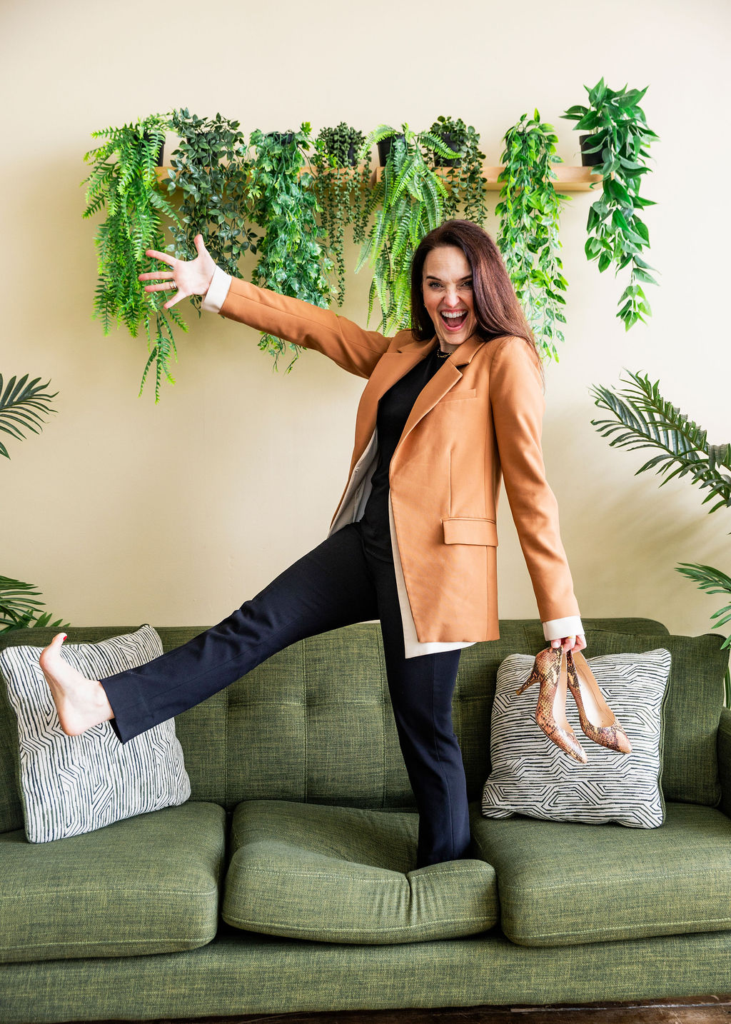 Sarah Walton smiling with her arms outstretched while standing barefoot on a green couch.