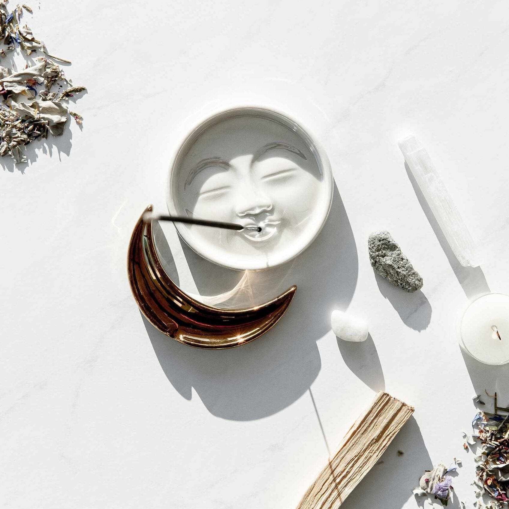 A moon-face bowl with burning incense, crystals, and palo santo in soft light